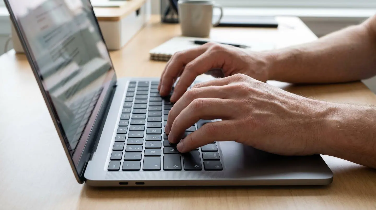 Gros plan sur une main tapant sur le clavier d'un ordinateur portable moderne posé sur un bureau lumineux, écran flou en arrière-plan
